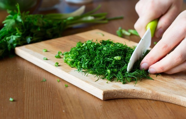 Mâini ale unui adult tăind verdețuri pe un tocător de lemn